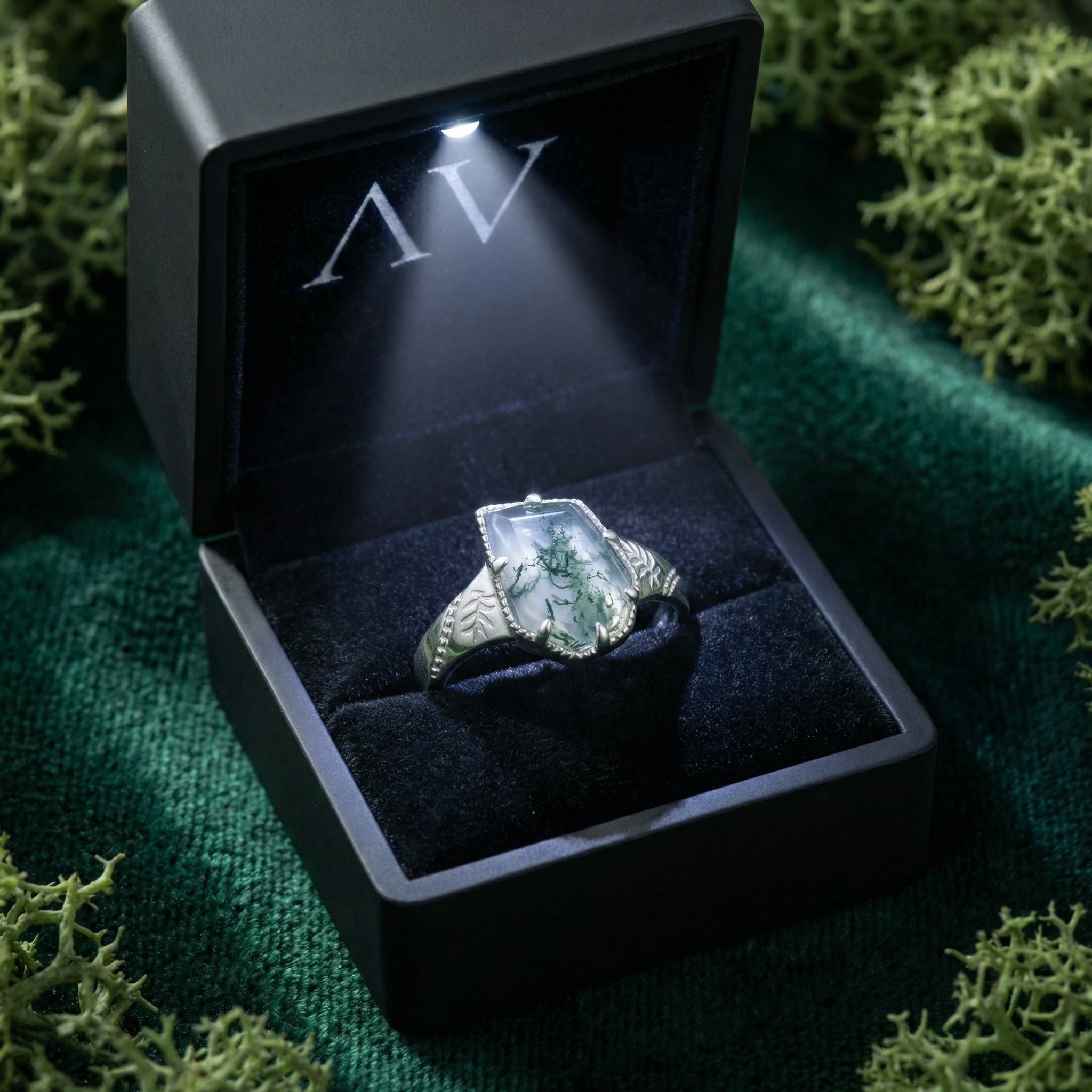 Moss agate sterling silver ring presented in a black light-up gift box on a green velvet background.