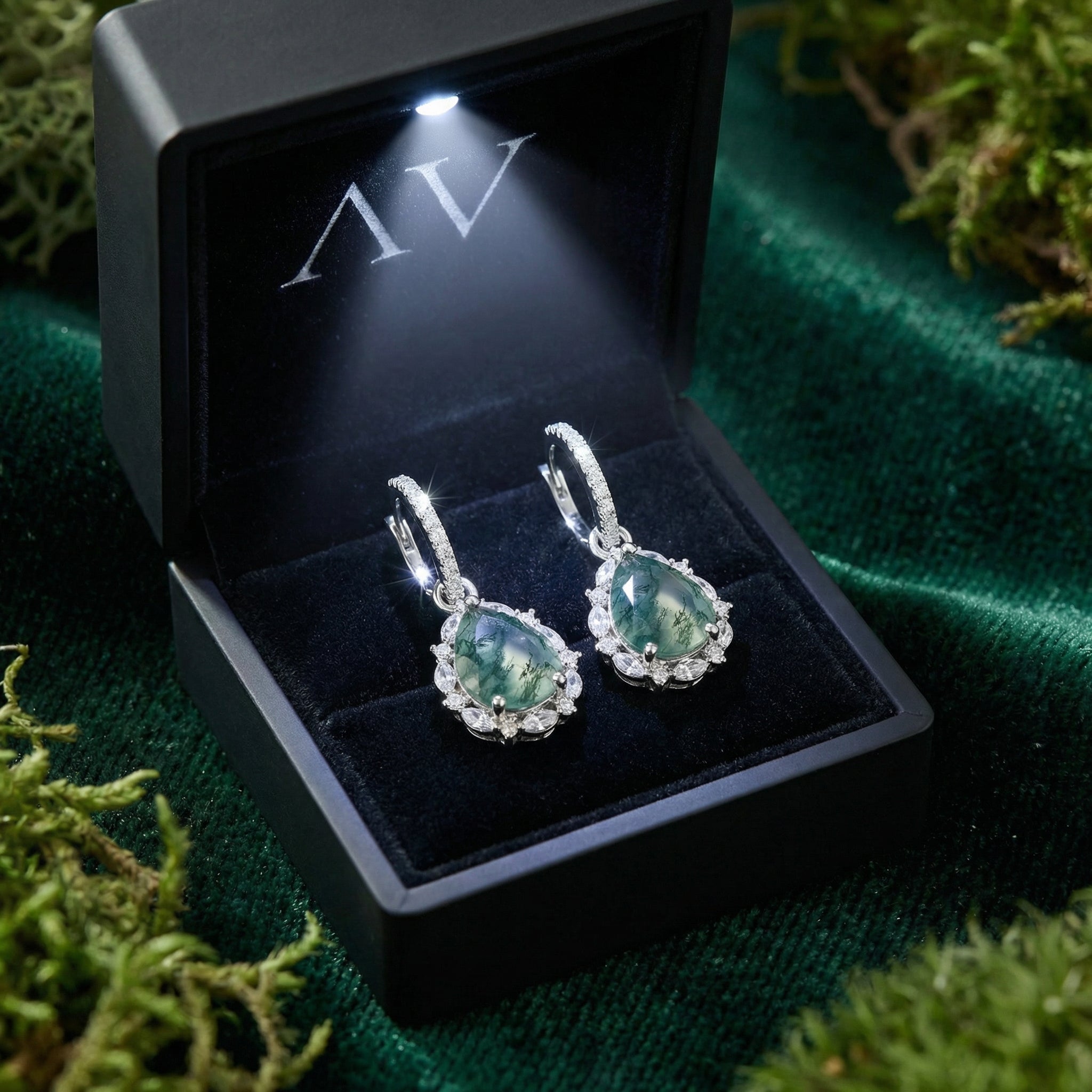 Teardrop moss agate sterling silver earrings presented in a black lighted gift box on a green velvet surface.