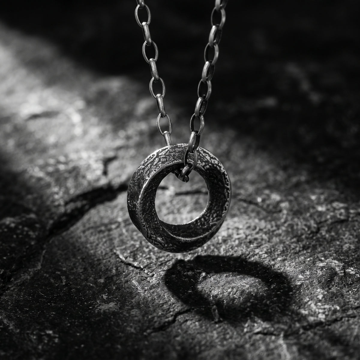 Textured silver ring pendant hanging from a link chain over a dark slate background.