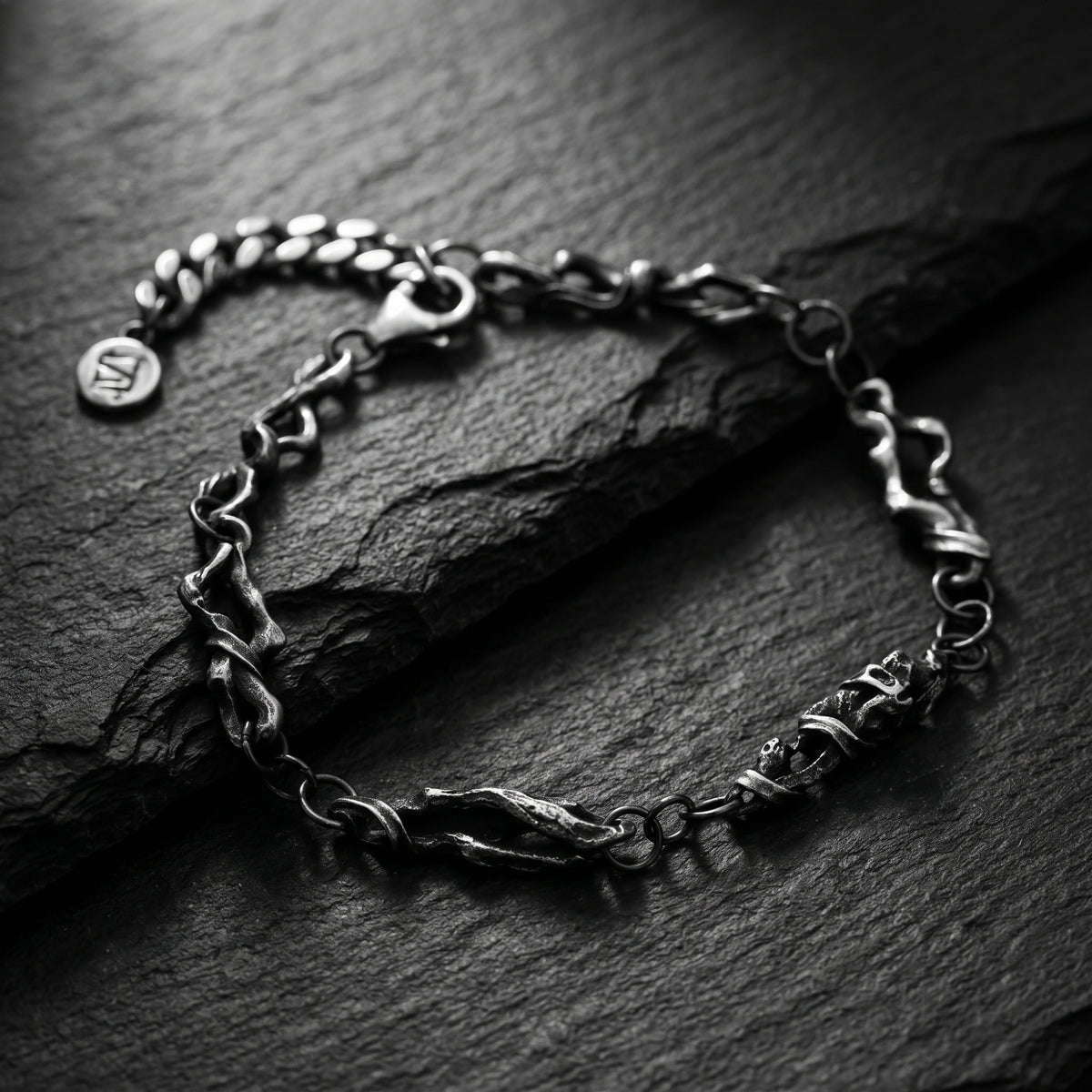 Close-up of the oxidized silver sculpted chain bracelet resting on dark slate, showing its textured links.