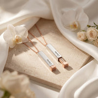 Two Adelise sliding bar necklaces in silver and rose gold stainless steel on stone with flowers.