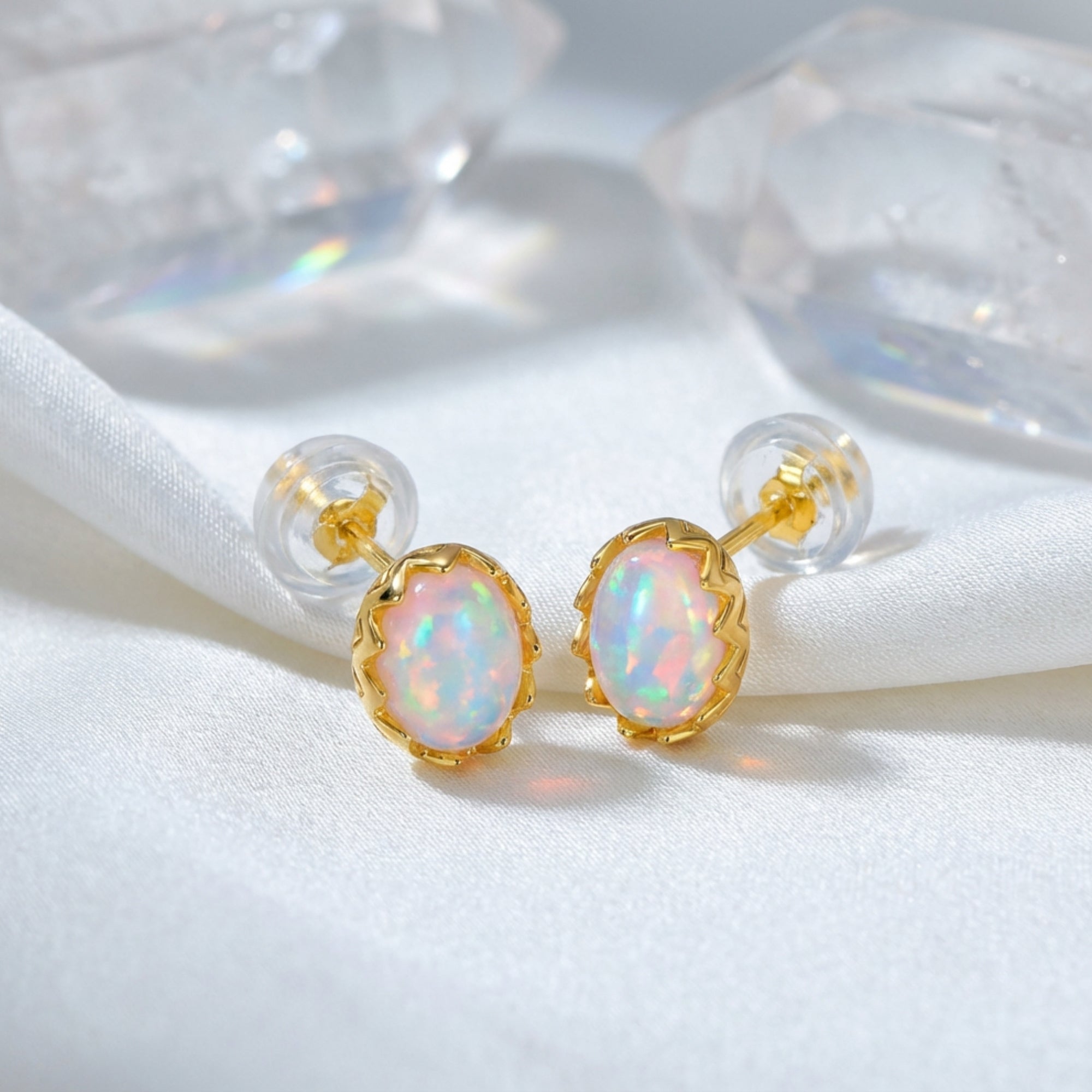 Yellow gold Novalie stud earrings with oval white opals resting on white silk with crystal props.