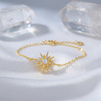Elowen starburst bracelet in gold-tone sterling silver with a round-cut white opal on white silk fabric.