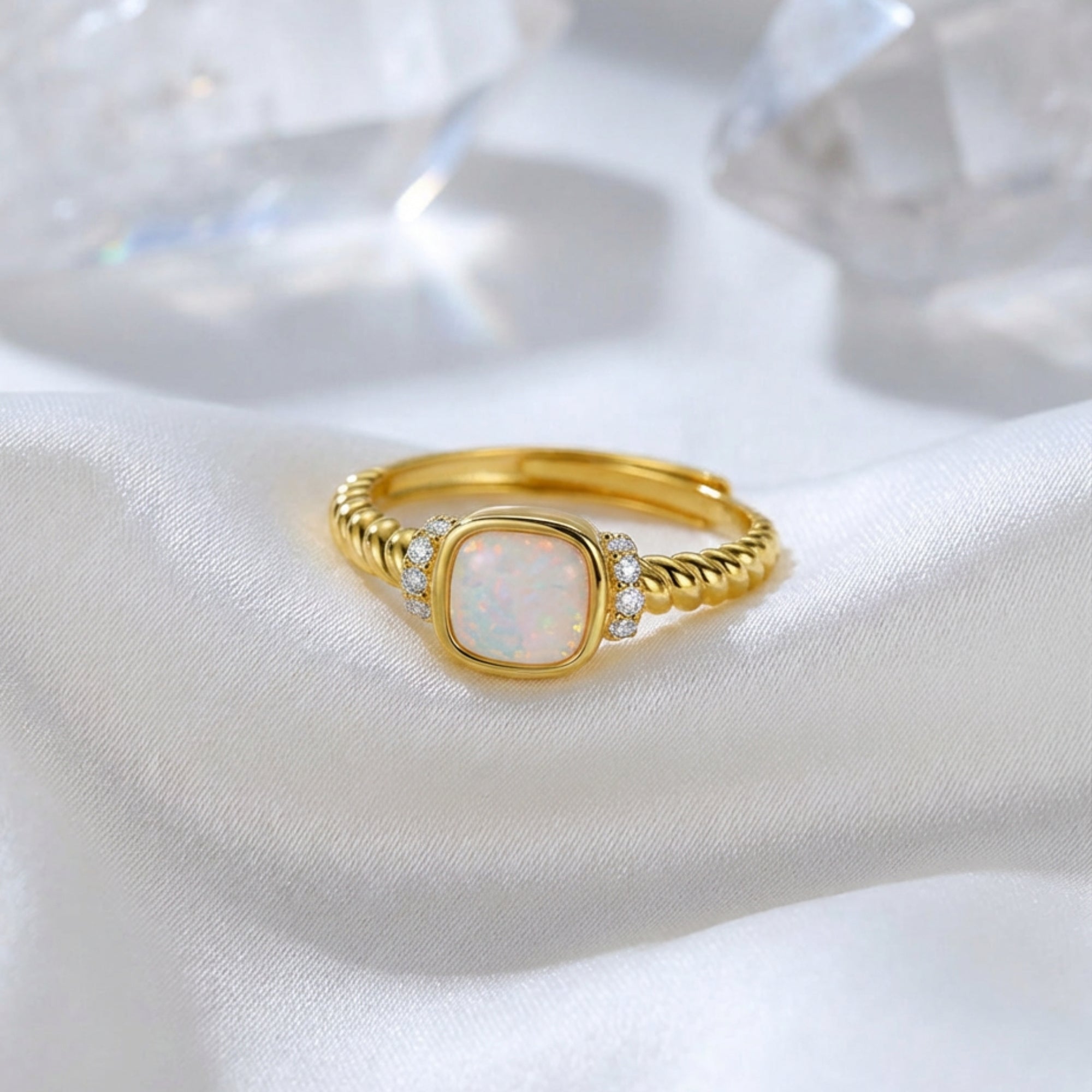 Gold-tone S925 silver Luminara ring with a cushion-cut white opal resting on white silk with crystals.