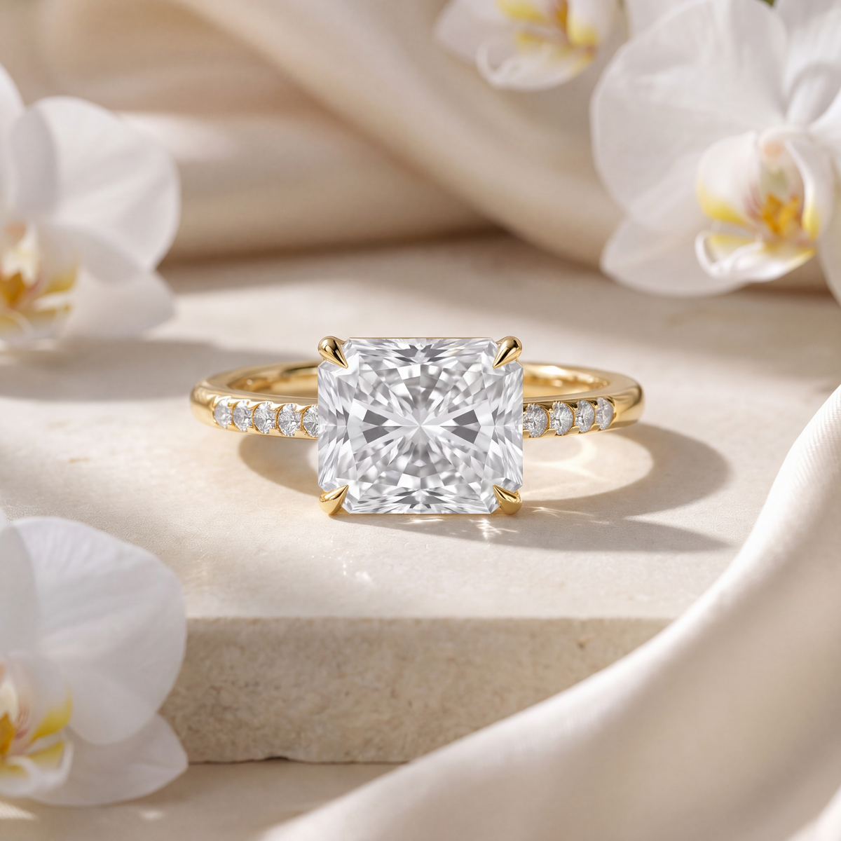 Yellow gold radiant cut moissanite engagement ring with a pavé band resting on a stone platform.