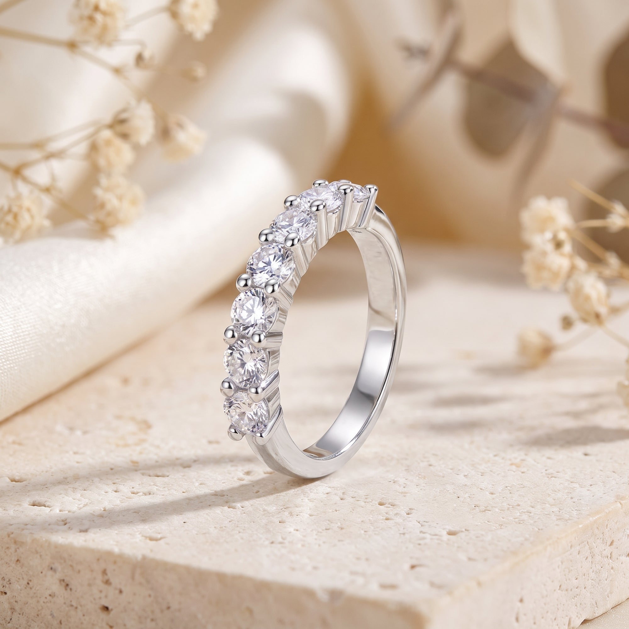 S925 sterling silver seven-stone eternity ring with round-cut stones on a stone surface with floral accents.