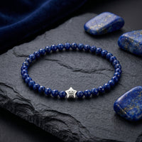 Faceted natural lapis bead bracelet with a sterling silver smiley star charm on a dark slate background.