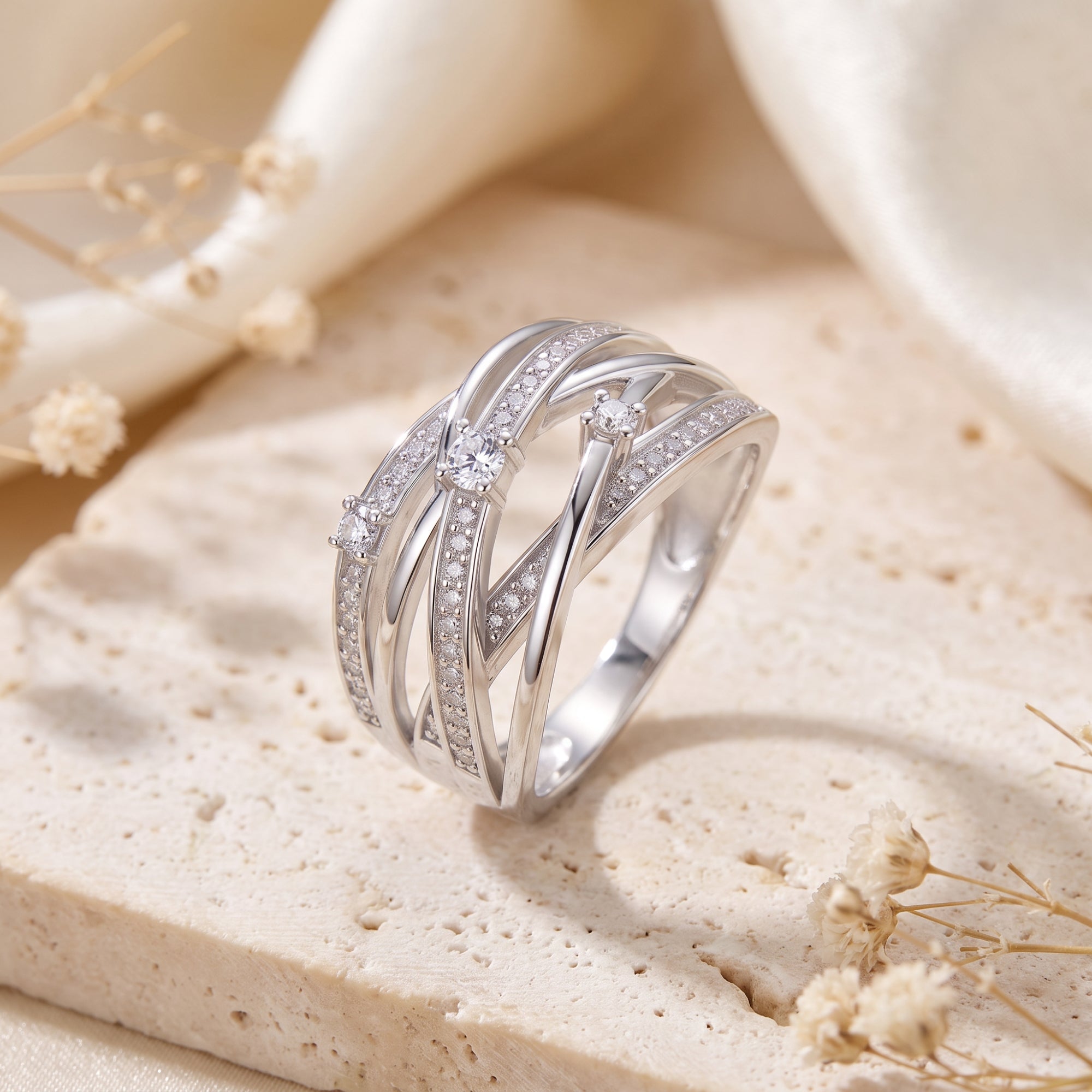 Sterling silver multi-row crossover ring with cubic zirconia on a styled stone background.