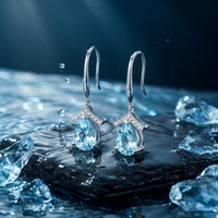 Pear cut natural aquamarine drop earrings in platinum on a wet stone with water splashes and ice crystals.