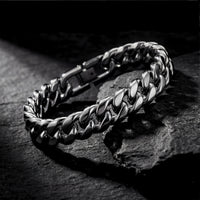 Silver 12mm stainless steel Cuban link bracelet resting on a dark textured rock surface.