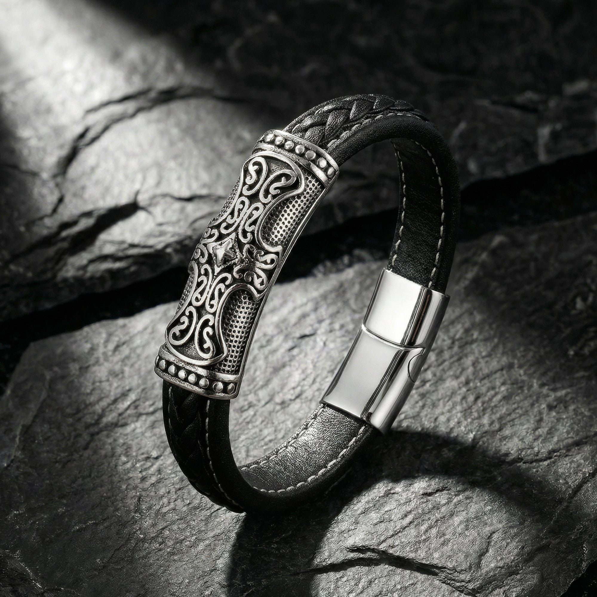 Runeforge men's black braided leather bracelet with an engraved 316L stainless steel clasp on a textured stone.