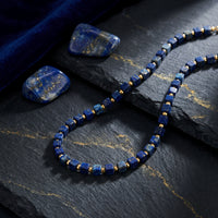 Sovereign Square natural lapis lazuli beaded necklace with gold-plated stainless steel on a stone background.