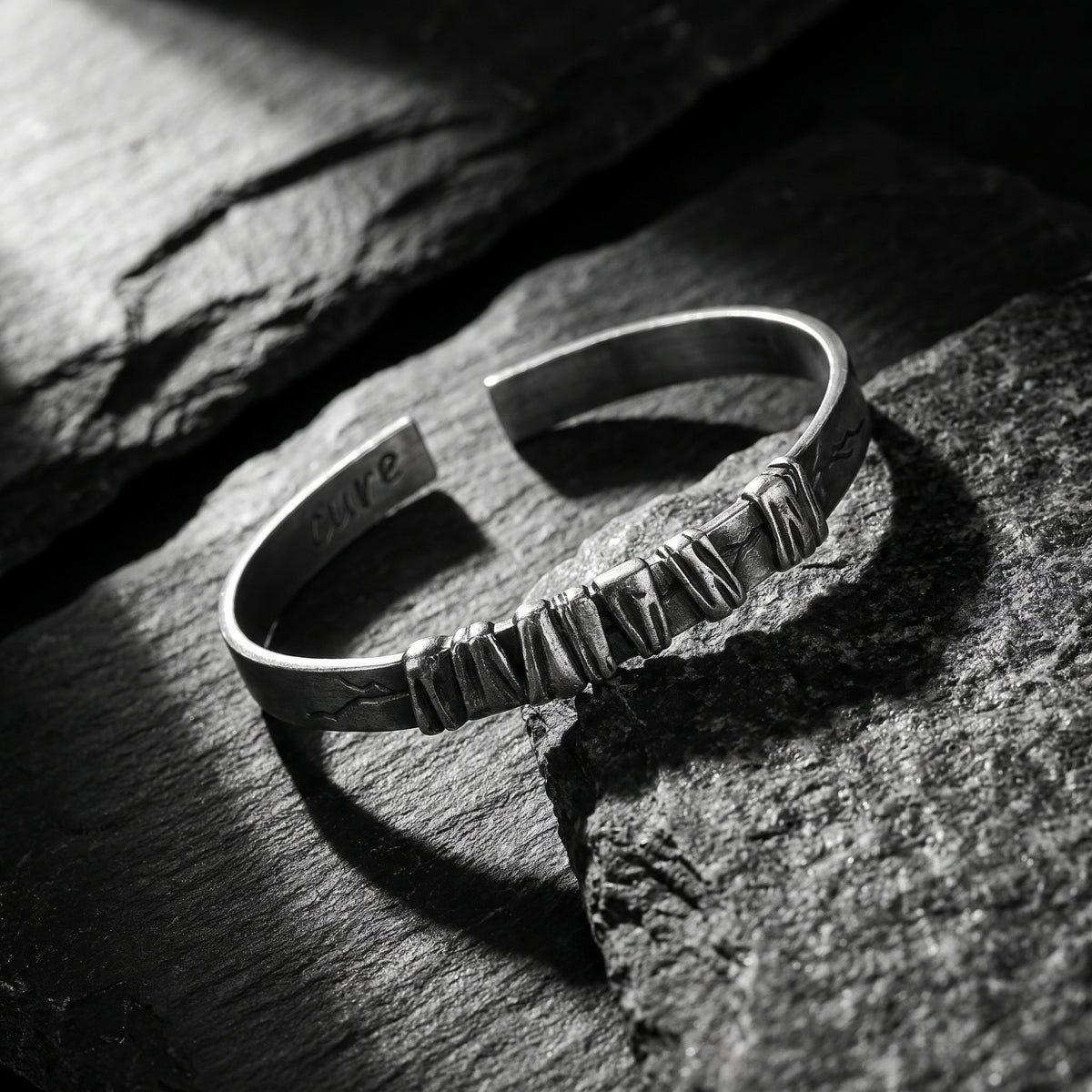 Angled view of an oxidized silver open cuff bracelet with sculpted segments, resting on dark slate.