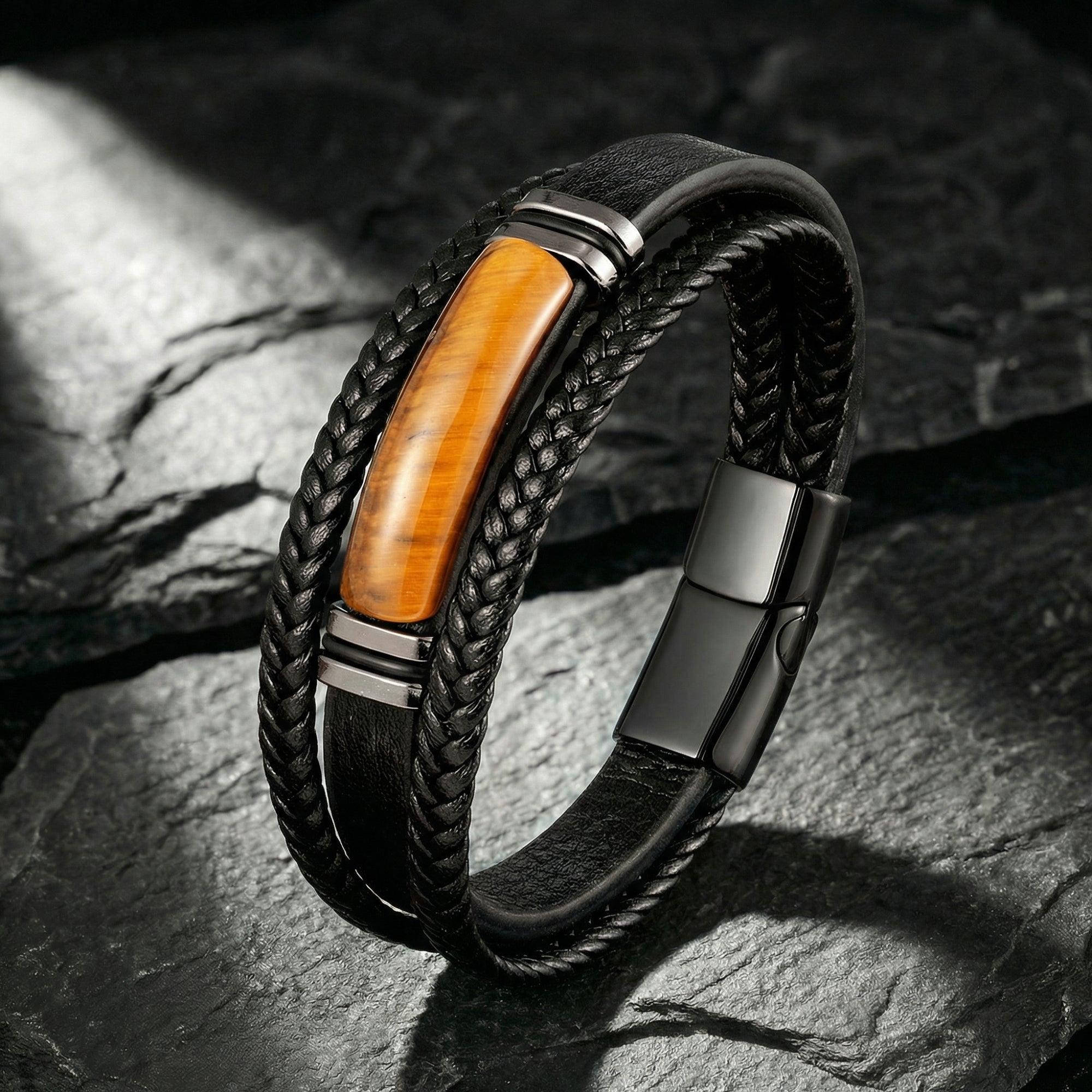 Black braided leather bracelet with tiger's eye stone and black stainless steel on a dark textured stone background.