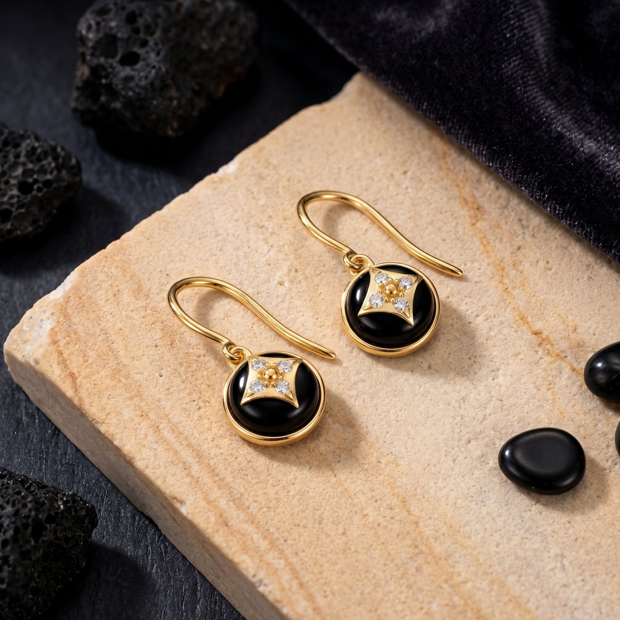 Yellow gold drop earrings with round black onyx and star-shaped diamond accents on a stone slab.