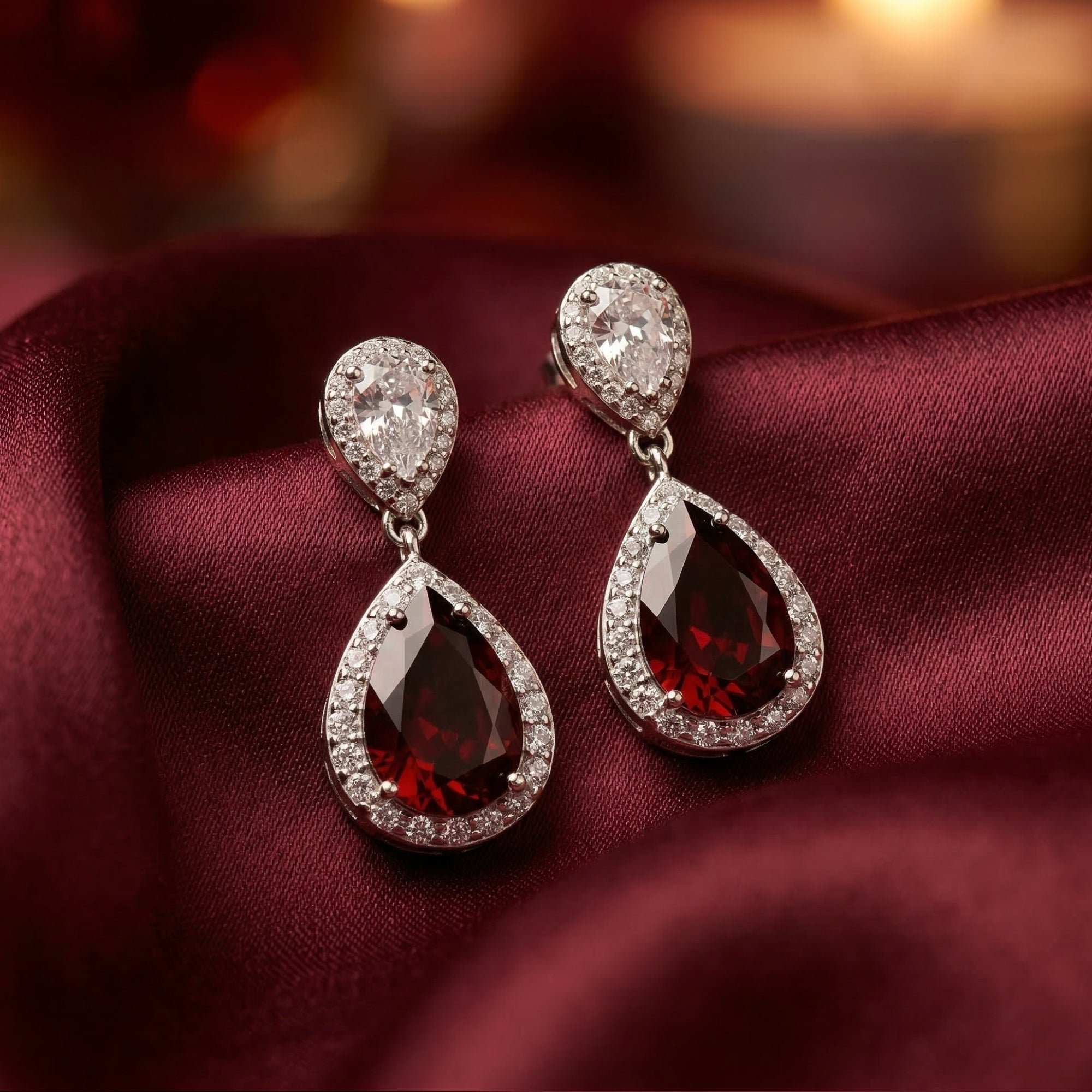 Rosaria drop earrings with pear-cut red garnets in silver halo settings resting on red silk.