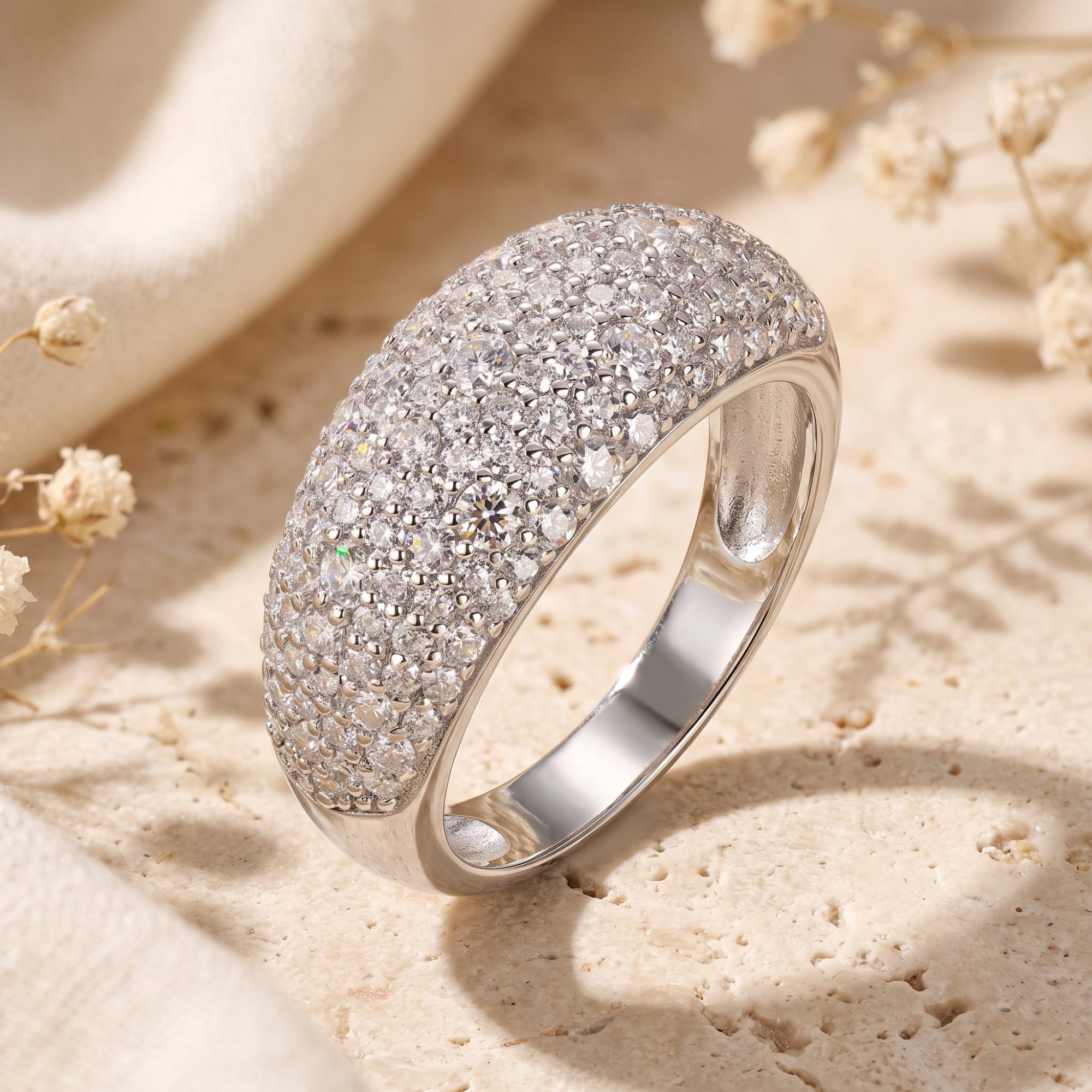 Silver dome ring with CZ micro-pave on a stone surface with dried flowers.