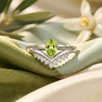 Front view of a natural pear cut peridot sterling silver ring with a V-shaped accent band on green silk fabric.