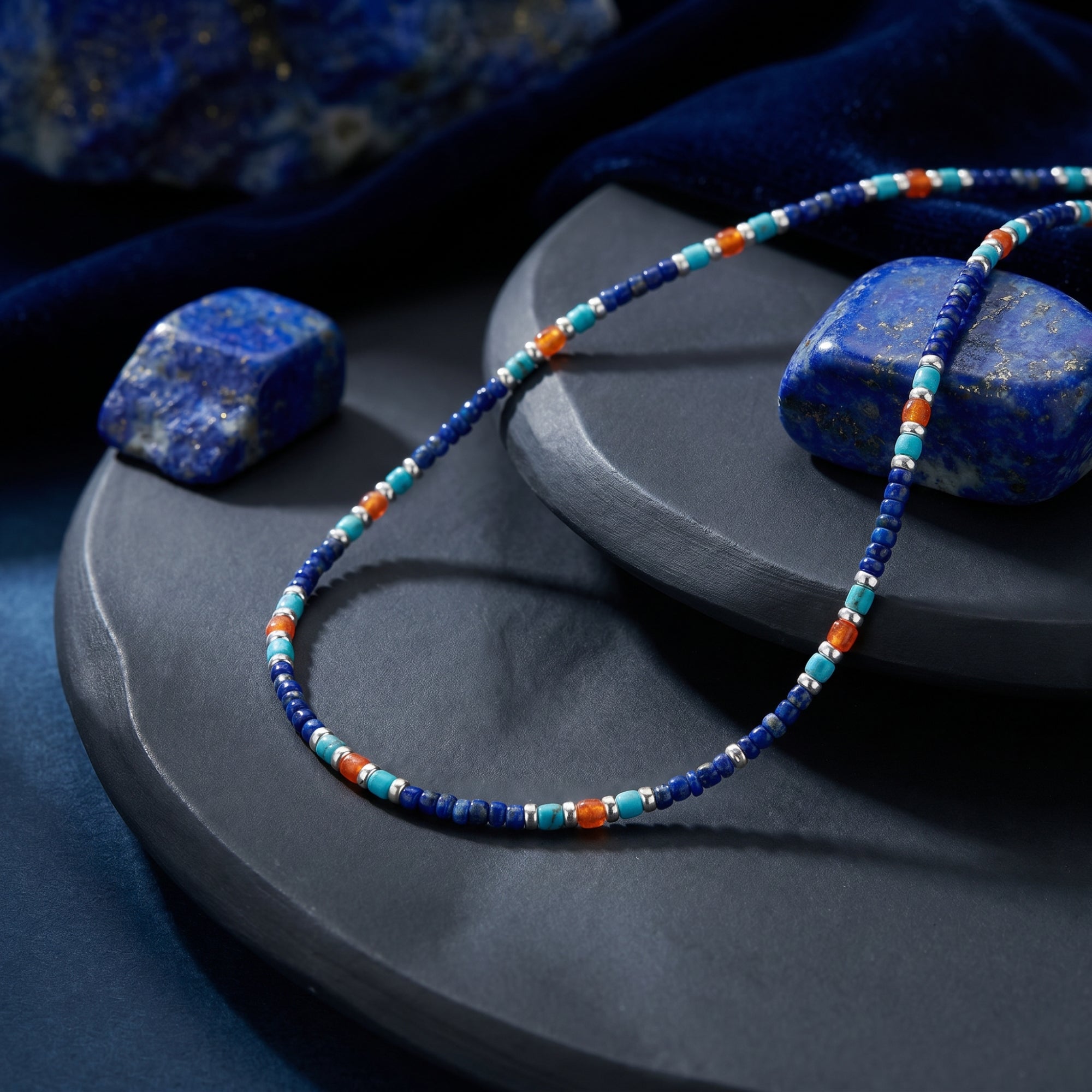Beaded necklace with 5mm lapis, turquoise, and orange beads and silver spacers on a stone plate.