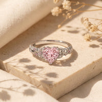 Silver heart-cut pink diamond ring on stone with dried flowers.