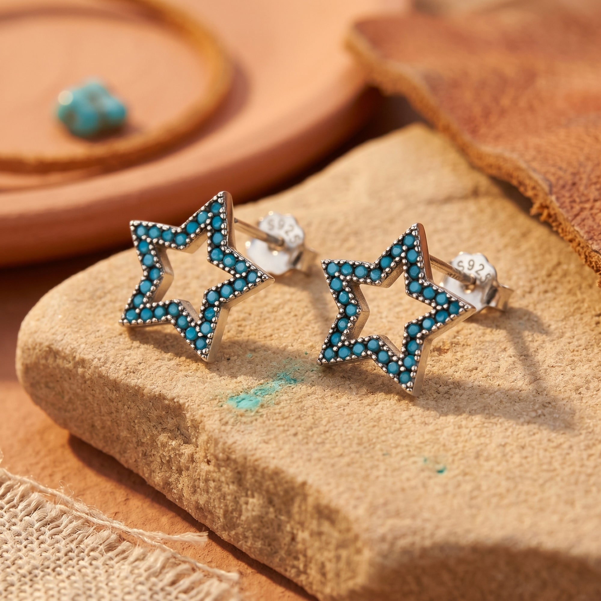 Silver star earrings with turquoise pave stones resting on a natural stone, showing the S925 sterling silver hallmark.