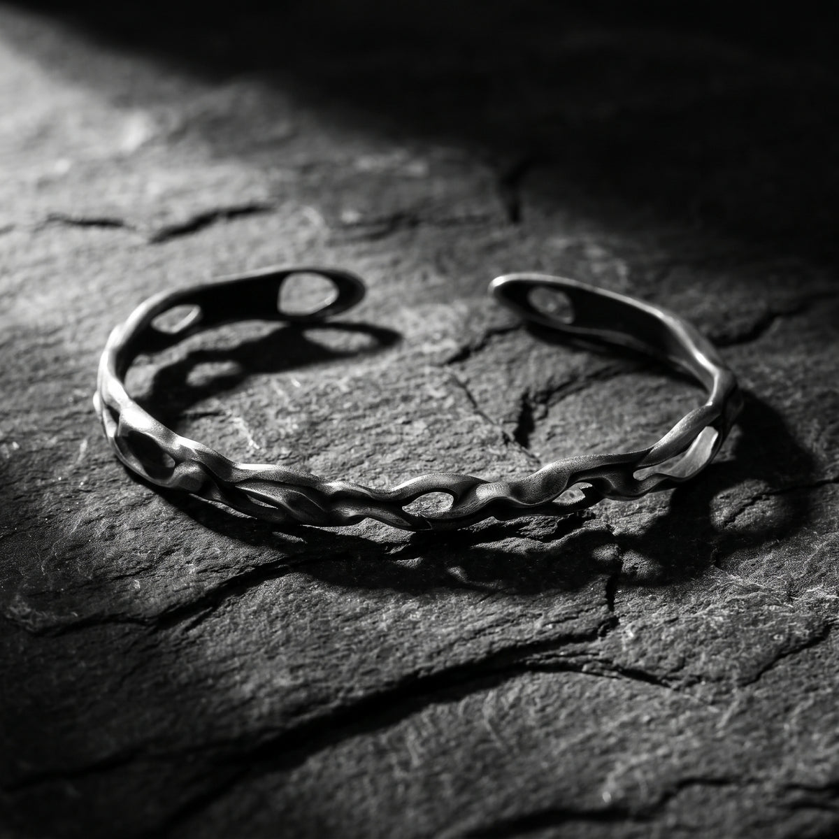 Sculpted silver wave cuff bracelet resting on dark slate, showing its open band design.