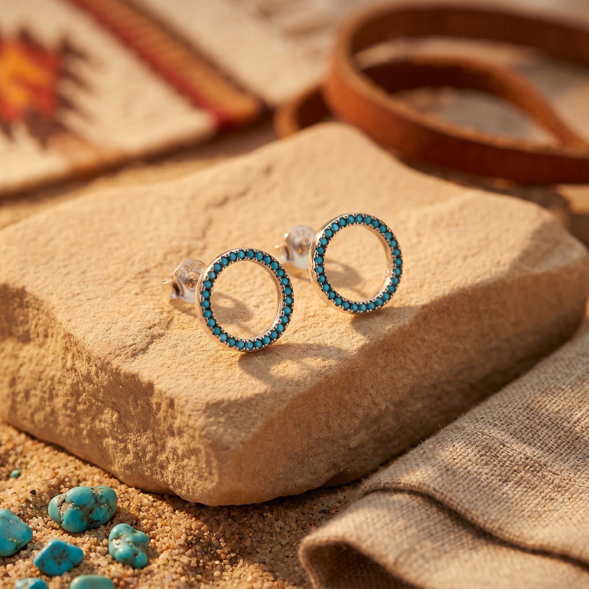 Silver circle earrings with turquoise stones resting on a desert rock in a lifestyle setting.