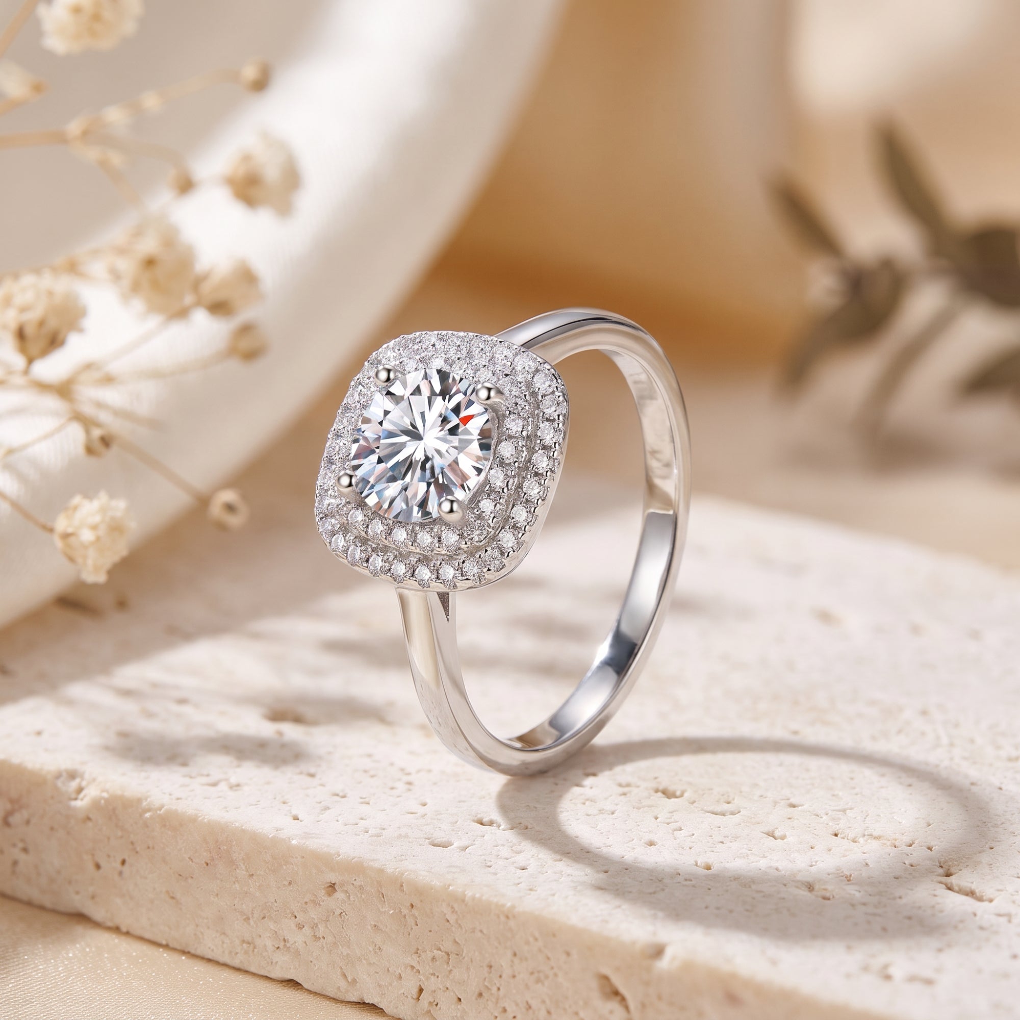 Sterling silver double cushion halo ring with a round cubic zirconia on a stone surface with flowers.