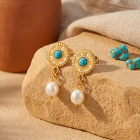 Gold turquoise and pearl drop earrings displayed on a desert rock with loose turquoise stones.