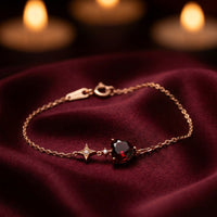18K rose gold heart-cut garnet bracelet with a star charm displayed on burgundy silk fabric.