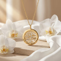 Gold tree of life pendant with simulated diamonds and engraved names, styled with white orchids.