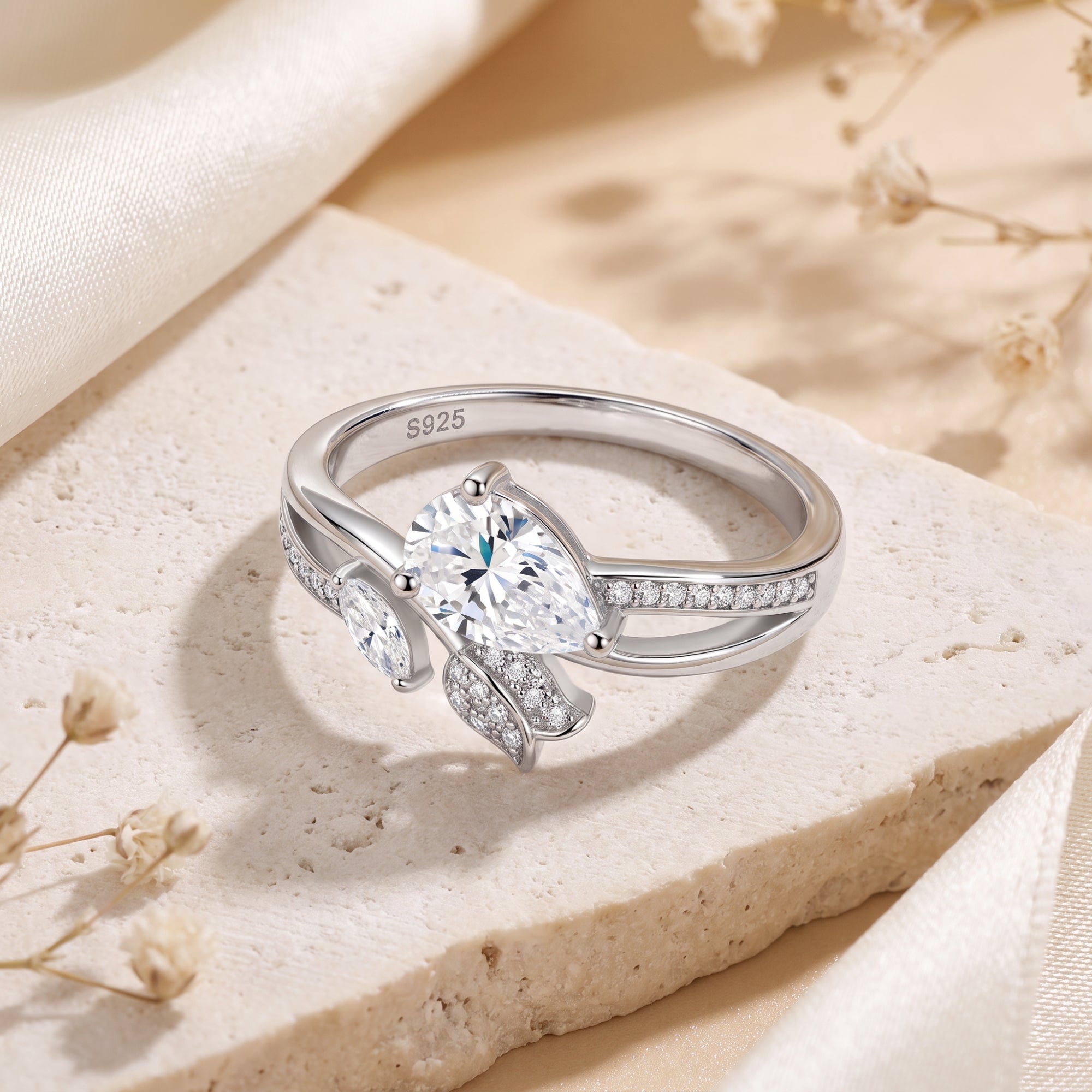 Silver willow leaf bypass ring with pear-cut simulated diamond on stone with dried flowers.
