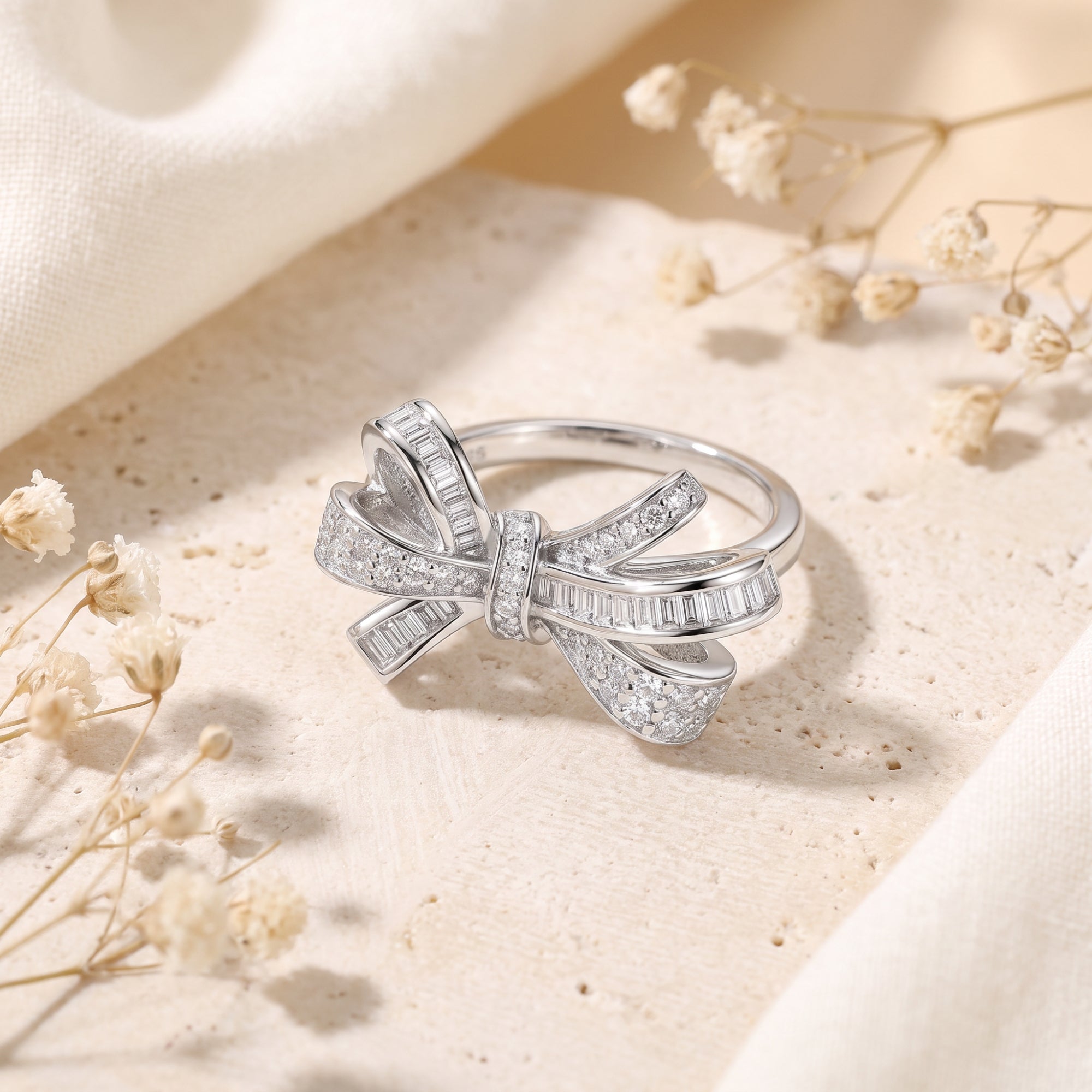 Sterling silver bow ring with baguette and pavé diamonds on a stone lifestyle background.