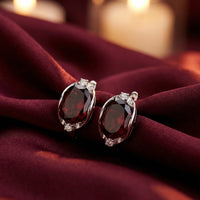 8x10mm oval cut garnet drop earrings in solid gold resting on burgundy silk with a warm candlelit background.