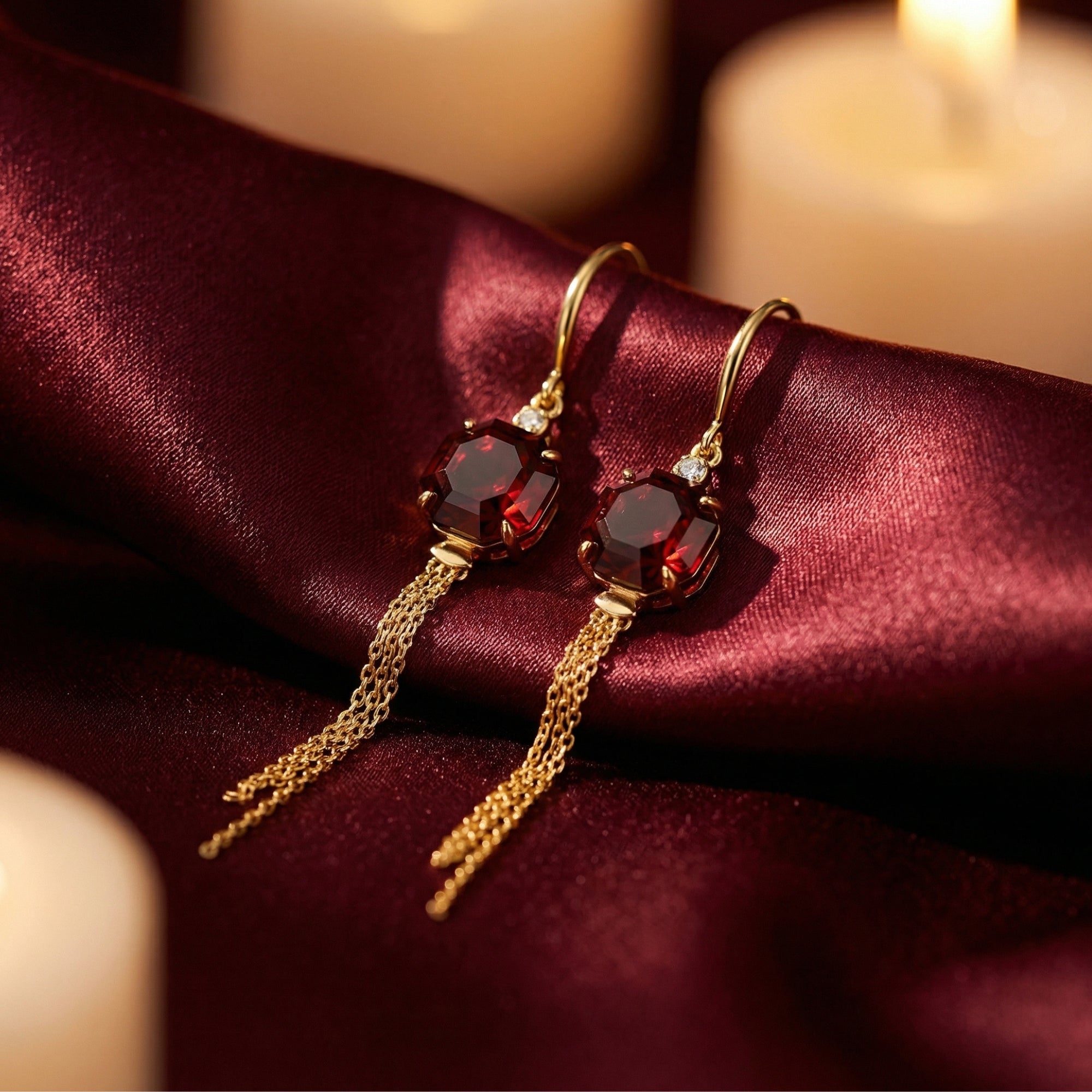 Octagon-cut garnet drop earrings in 18K yellow gold with chain tassels styled on red satin fabric.