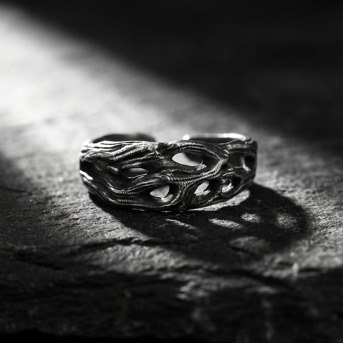 Close-up front view of the textured openwork silver ring resting on a rough slate surface.