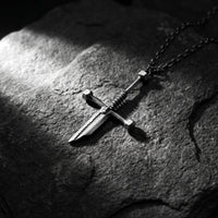 Silver dagger pendant and chain lying diagonally on a rough dark rock surface.