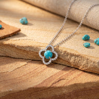 Silver quatrefoil necklace with round turquoise cabochon on a textured stone background.