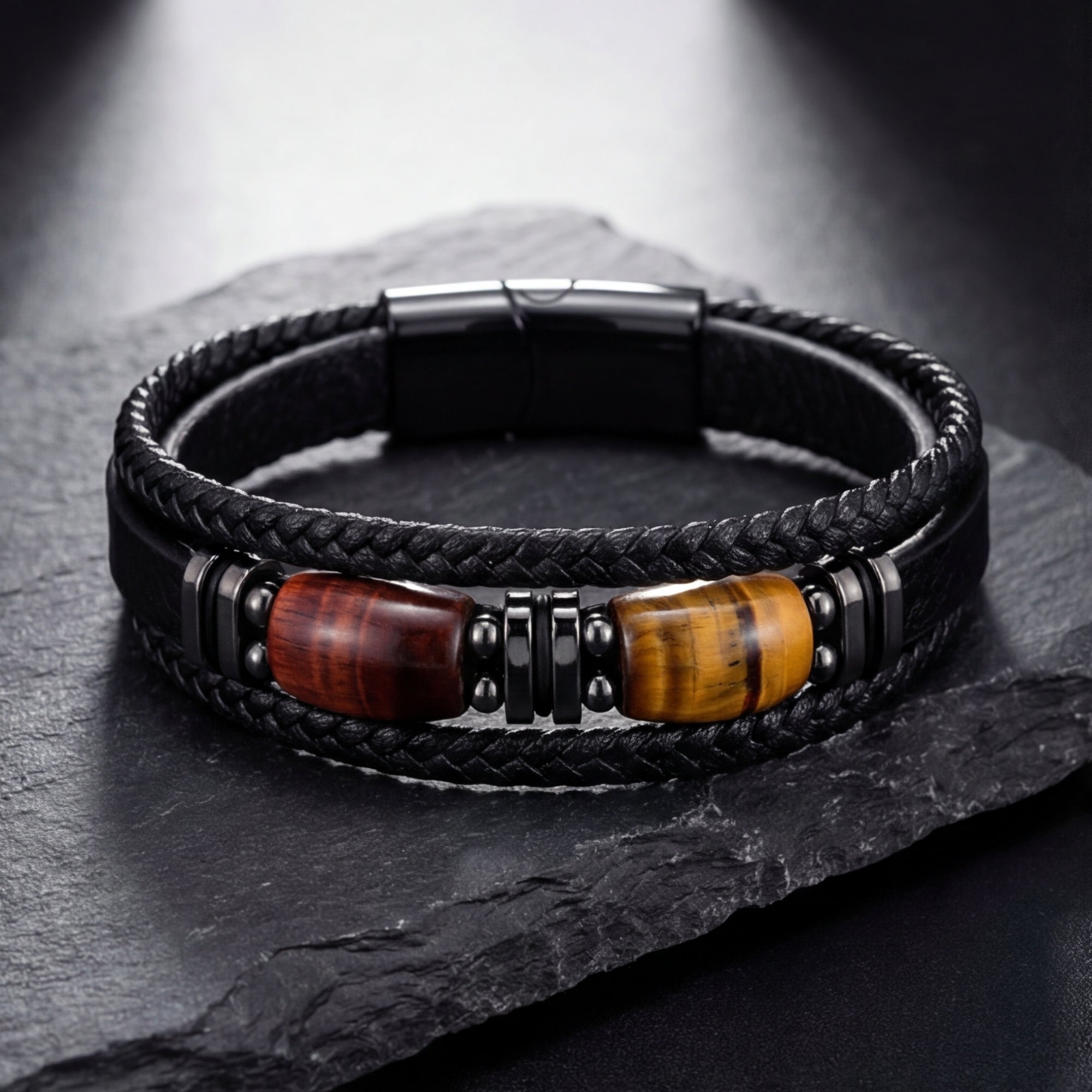 Braided black leather bracelet with tiger's eye barrel beads and black steel accents on a dark slate surface.