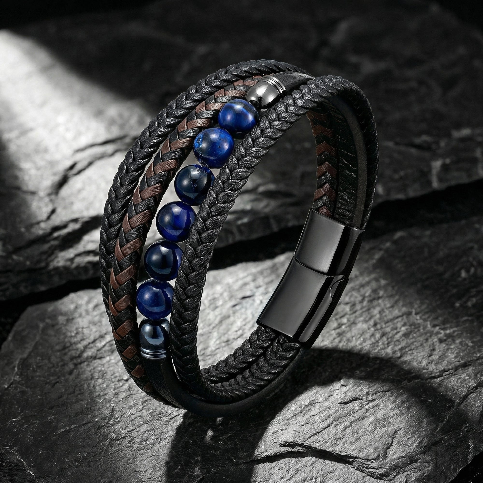 Multi-layered black leather bracelet with blue beads and black stainless steel clasp on a textured stone surface.