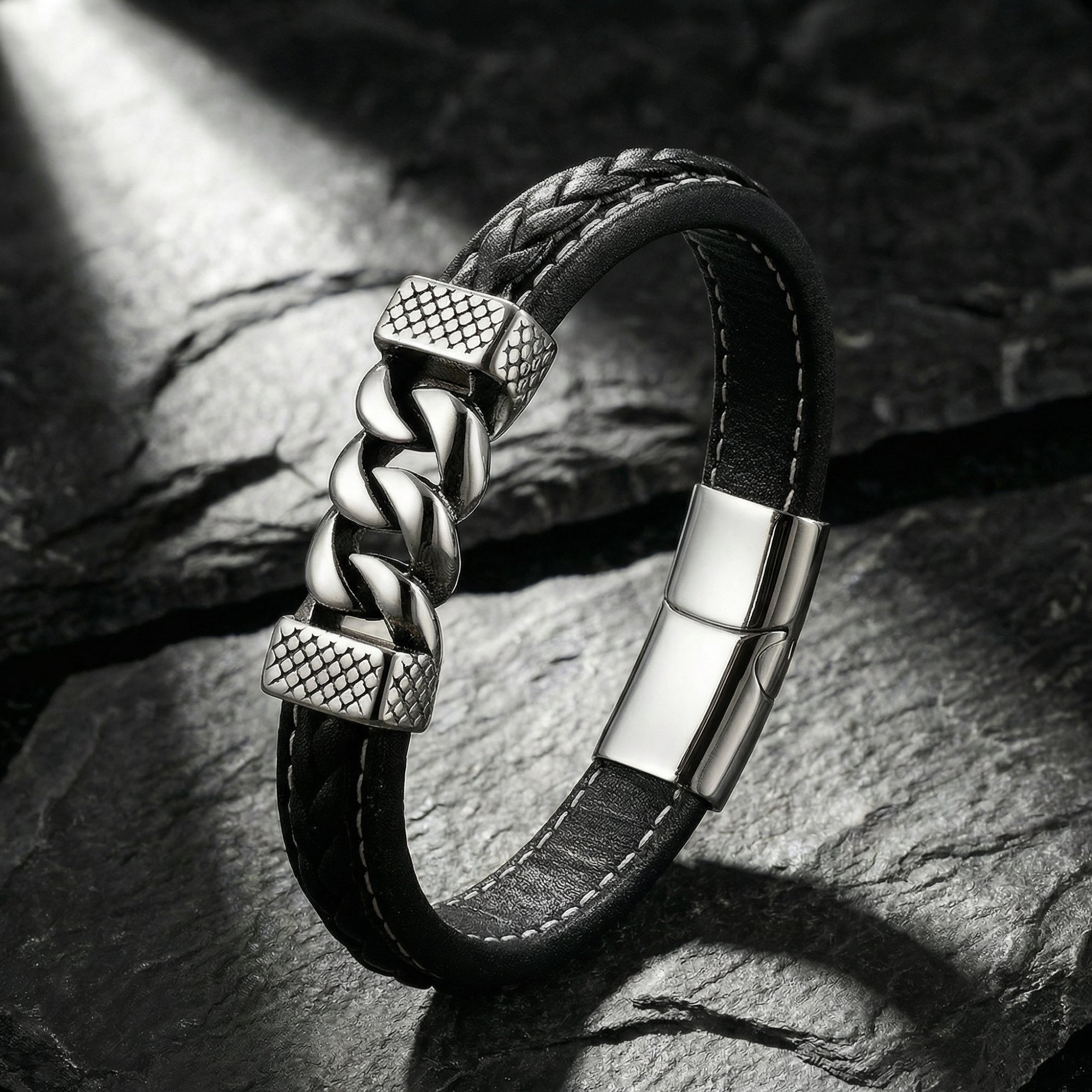 Braided black leather bracelet with silver stainless steel links standing on a dark textured rock background.