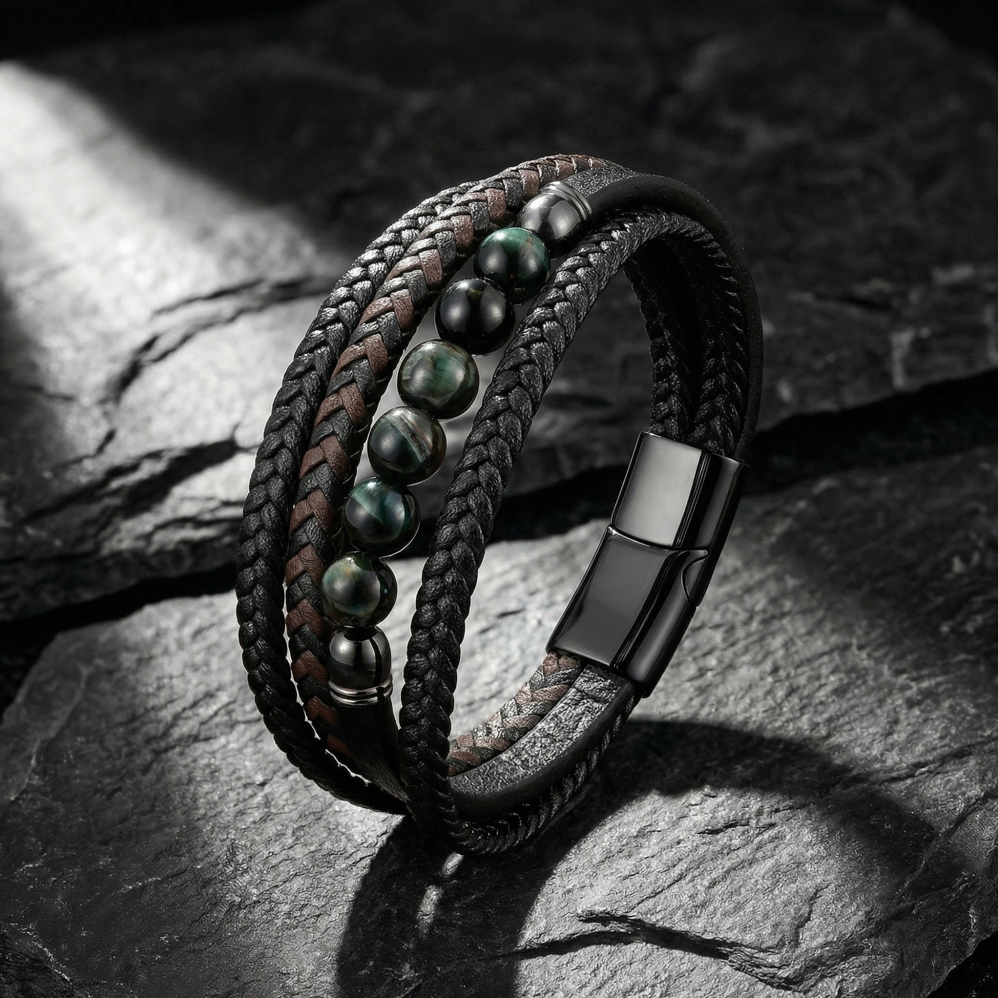 Multi-layered black and brown braided leather bracelet with round green beads and black stainless steel clasp on stone.