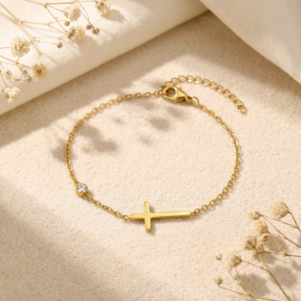 Gold-tone chain bracelet with a horizontal cross and bezel-set cubic zirconia, shown flat with clasp and extender visible.