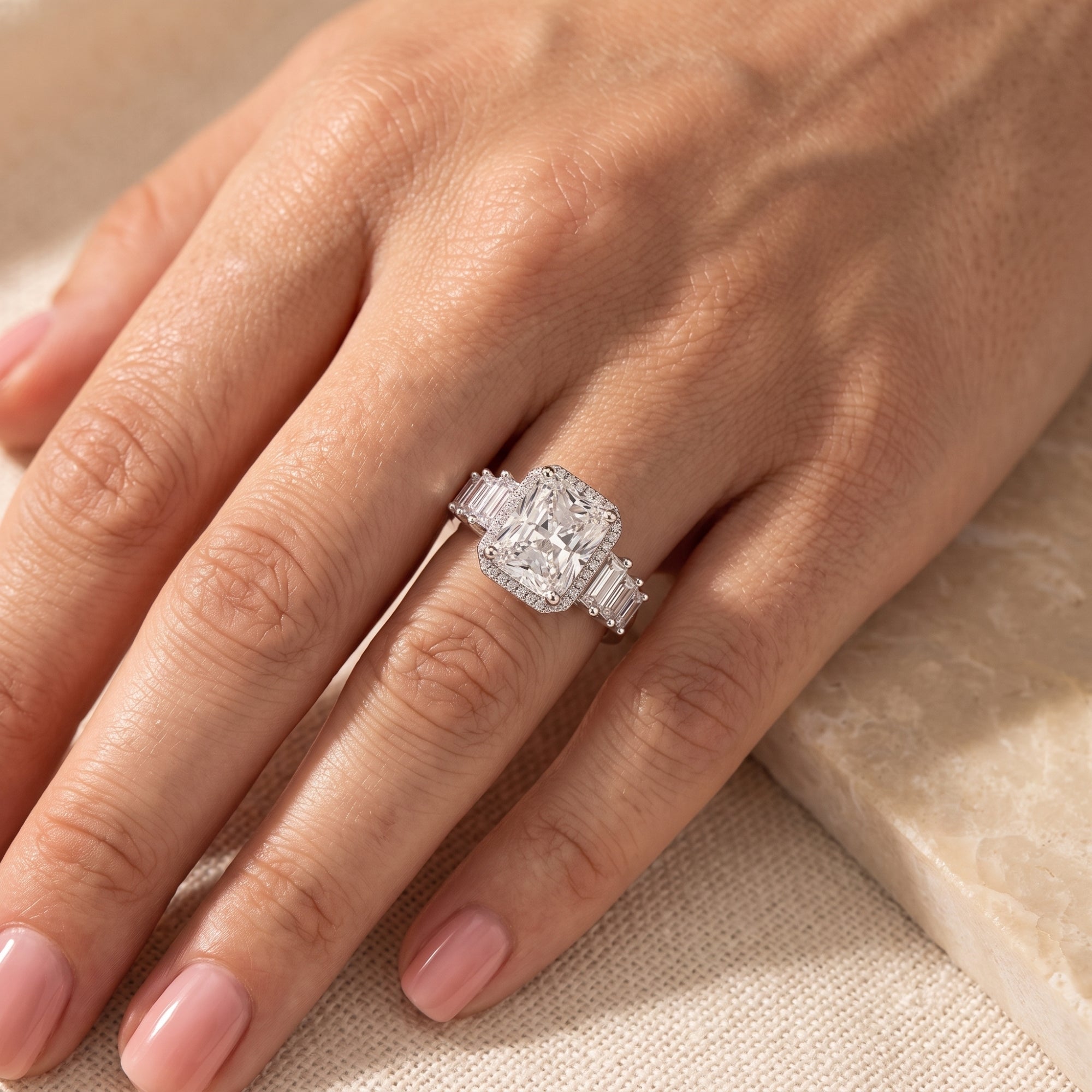 Sterling silver cushion-cut halo ring with baguette side stones worn on a hand.