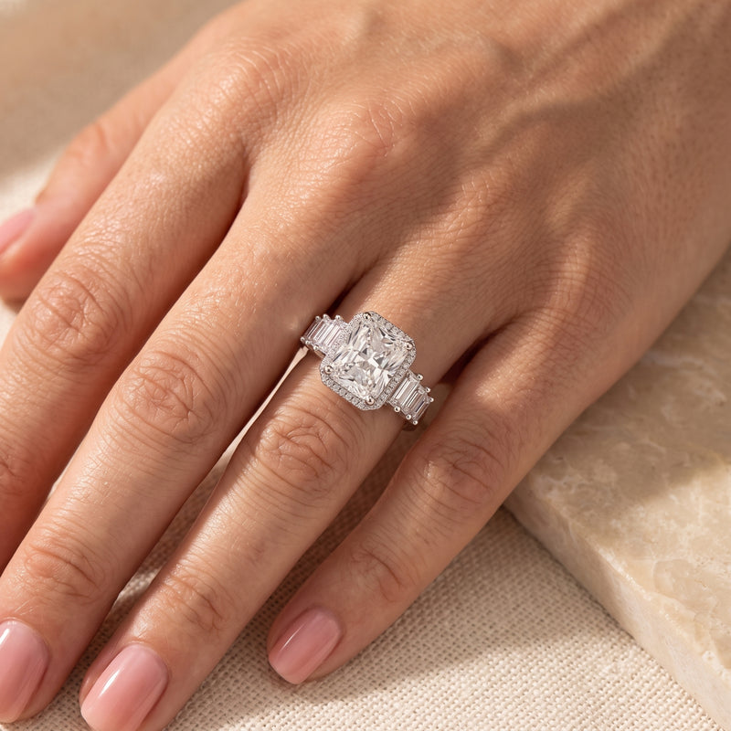 Sterling silver cushion-cut halo ring with baguette side stones worn on a hand.