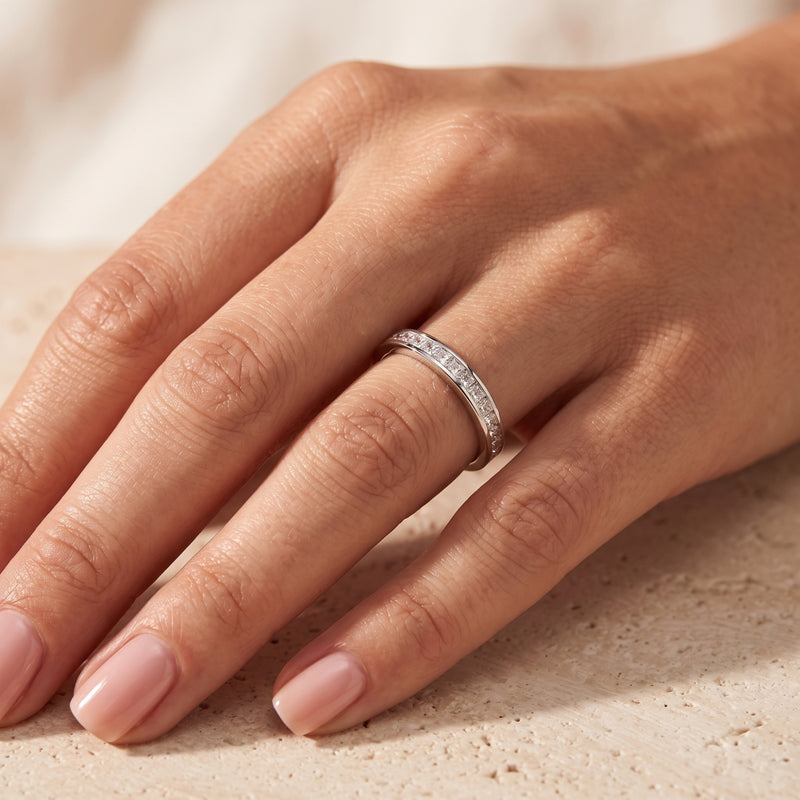 Sterling silver princess cut cubic zirconia eternity band worn on a model's ring finger.