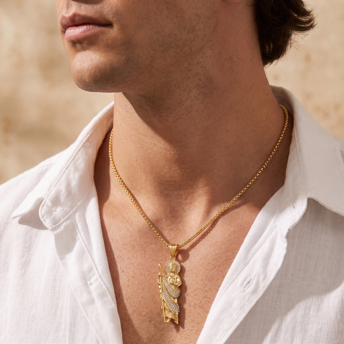 Model wearing a gold-tone St. Jude pendant necklace with an open white linen shirt.