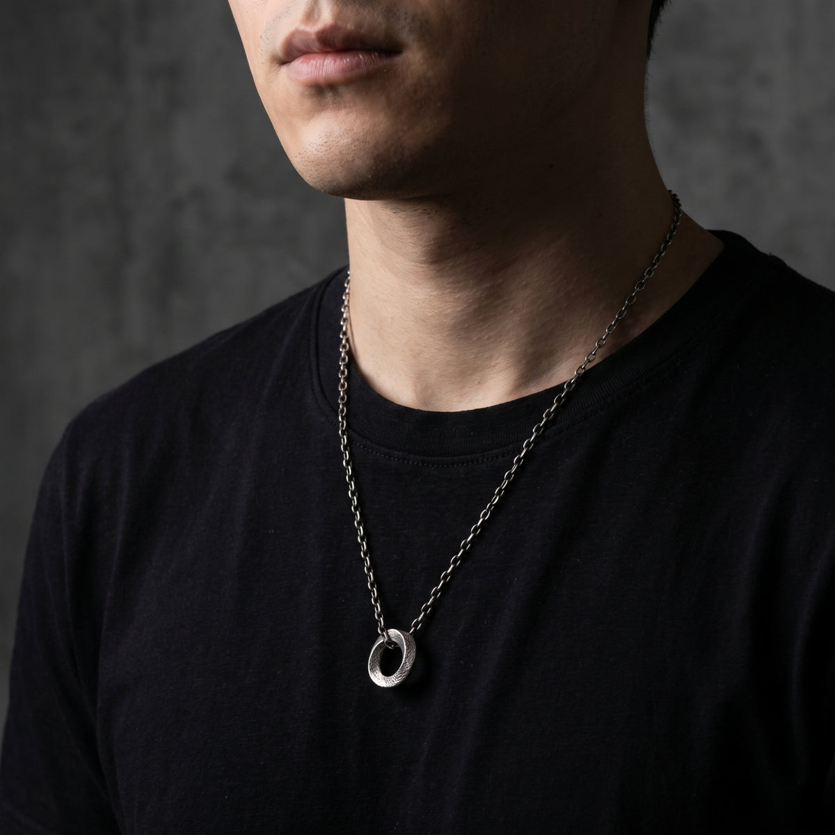 Front view of a model wearing the textured silver circle pendant necklace over a black T-shirt.