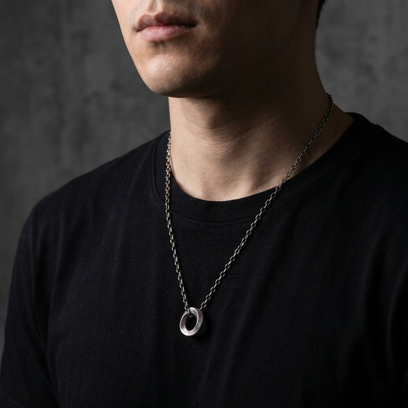 Front view of a model wearing the textured silver circle pendant necklace over a black T-shirt.
