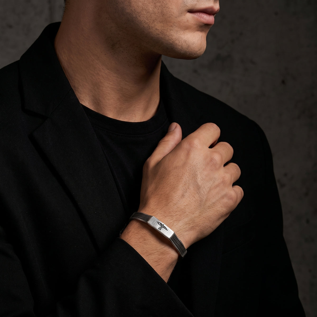 Silver grooved raven cuff bracelet worn on a man's wrist with a black suit jacket and tee.